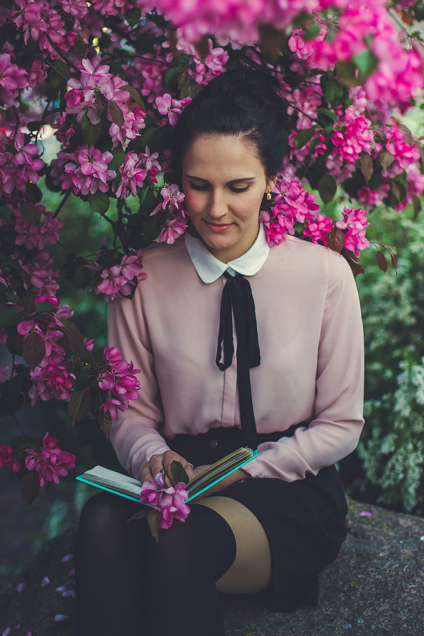 Woman reading book under blooming pink flowers