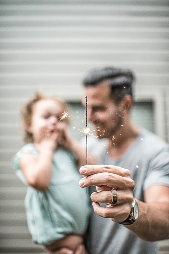 Father holding sparkler with daughter in background