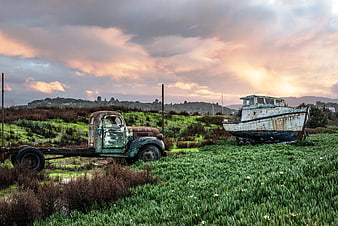 Rusty vintage truck and abandoned boat in green field at sunset