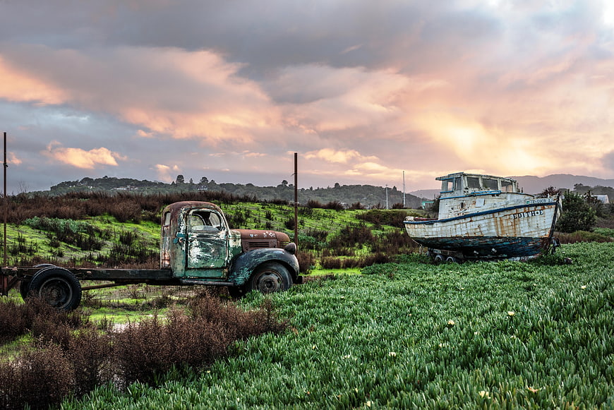 Rusty vintage truck and abandoned boat in green field at sunset