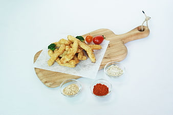 Fried chicken strips on wooden board with spices and vegetables