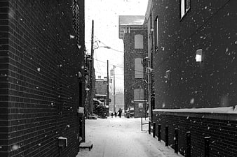 Black and white photo of snow falling in a narrow urban alleyway