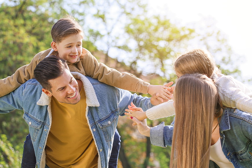 Happy family playing piggyback in sunny park