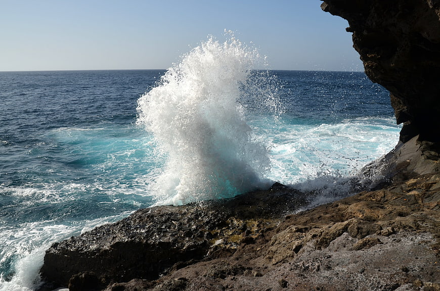 Powerful ocean wave crashing against rocky coastal cliff