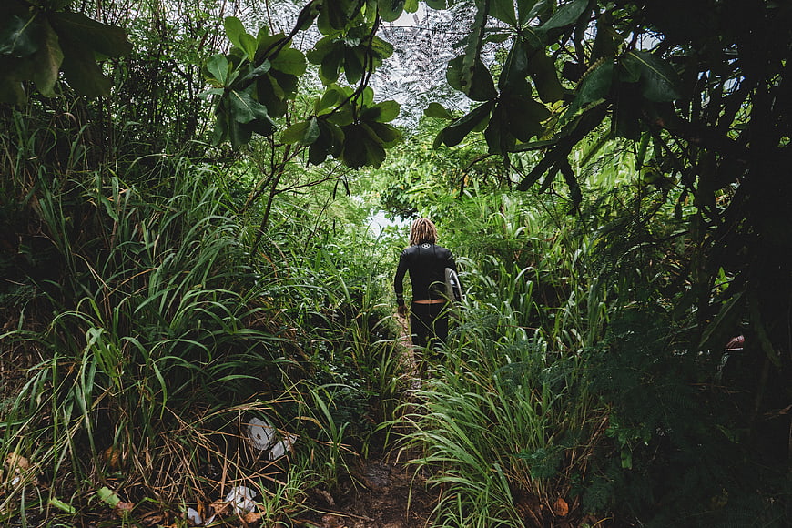 Surfer in Wetsuit Walking Through Jungle Path
