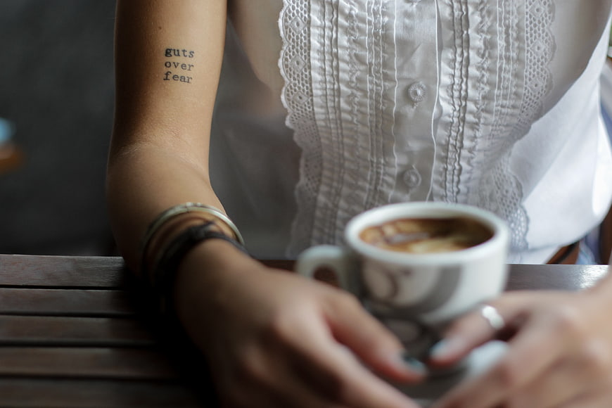 Woman with Guts Over Fear Tattoo Holding Coffee Cup