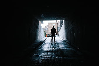 Silhouette of Man Walking Through Dark Tunnel