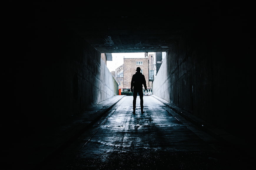 Silhouette of Man Walking Through Dark Tunnel