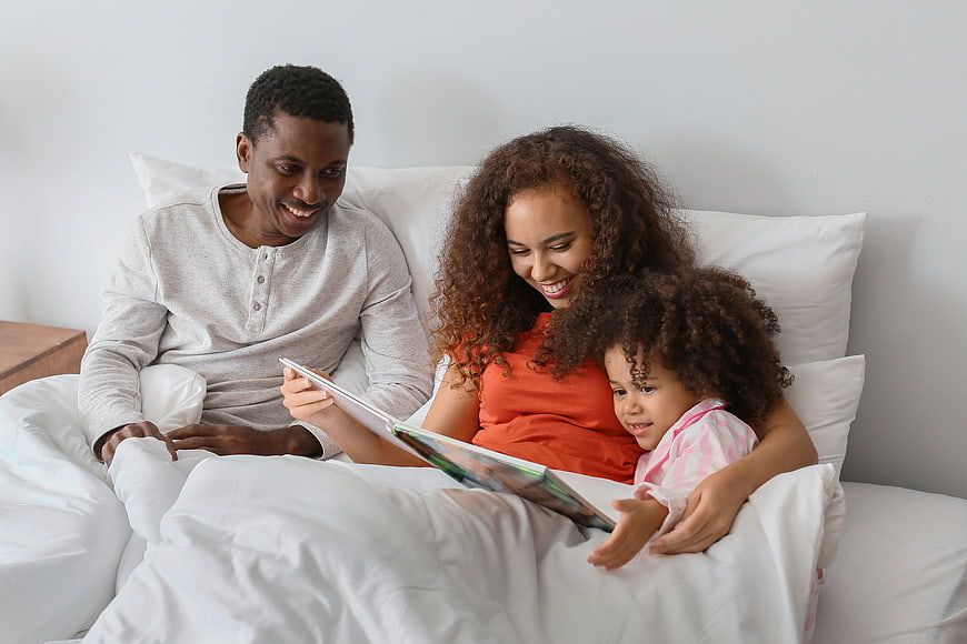 Happy African American Family Reading Book in Bed