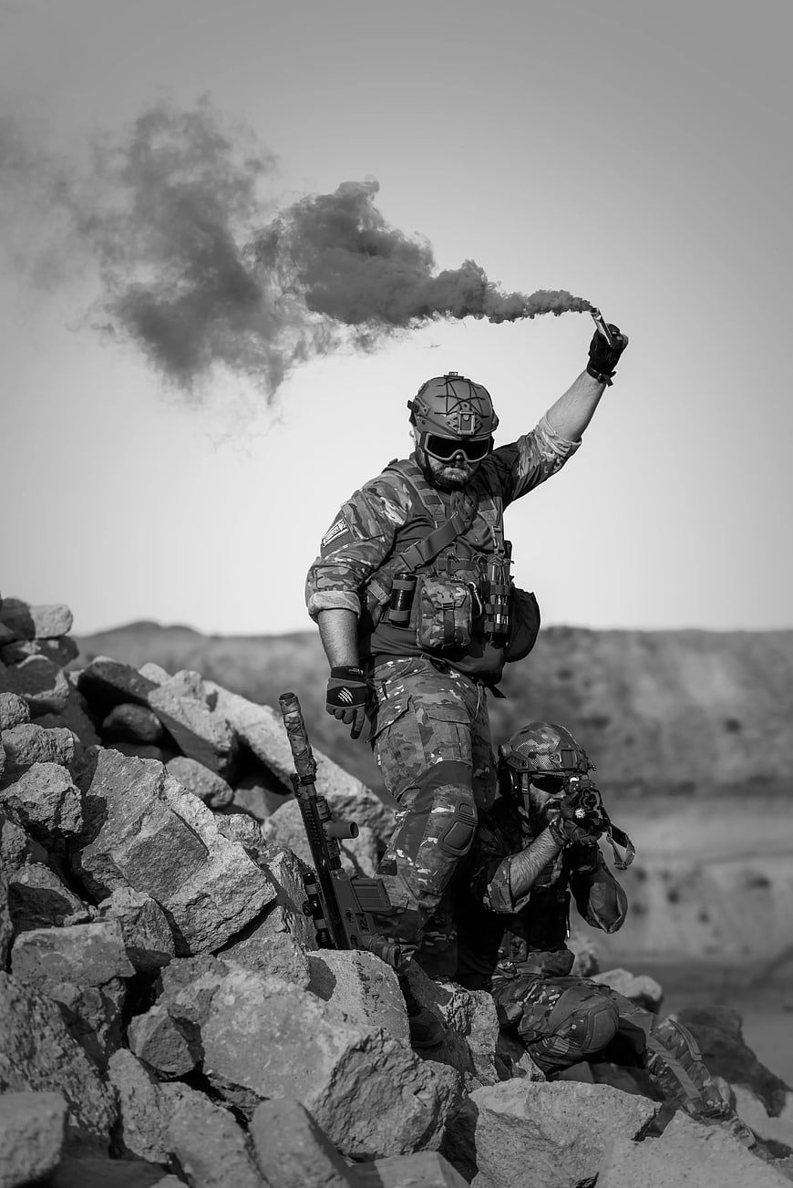 Soldier holding smoke flare on rocky terrain