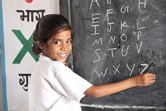 Smiling young school girl writing alphabet on blackboard