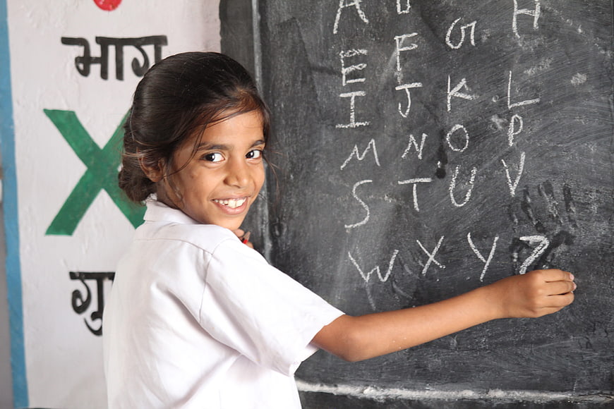 Smiling young school girl writing alphabet on blackboard