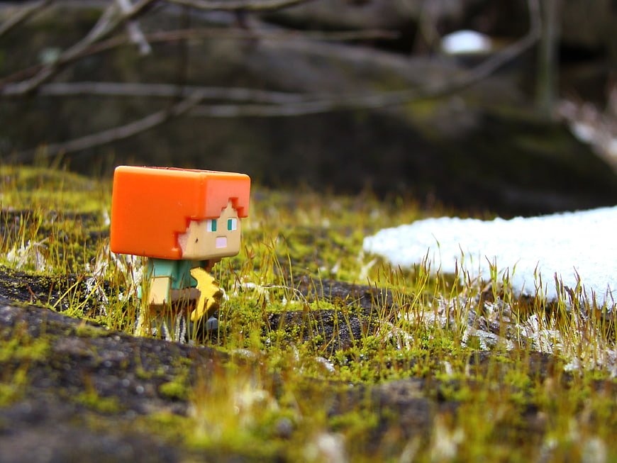 Minecraft Alex figurine standing on mossy rock with snow