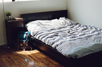 Unmade bed with striped duvet and backpack in sunlit room