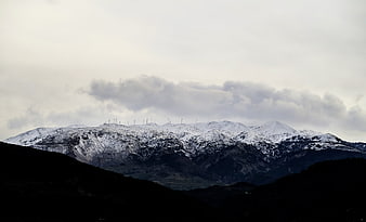Snow-Capped Mountain Range with Wind Turbines Under Cloudy Sky
