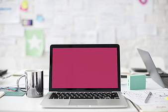 Modern workspace with laptop displaying pink screen and office supplies