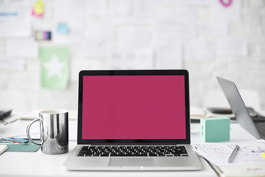 Modern workspace with laptop displaying pink screen and office supplies