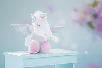 Sleeping white plush unicorn with wings on a pastel blue table