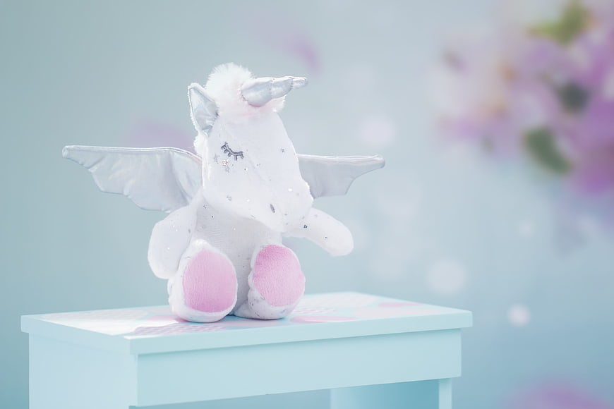 Sleeping white plush unicorn with wings on a pastel blue table
