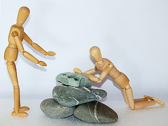 Wooden Mannequins Helping Each Other Over Stacked Stones