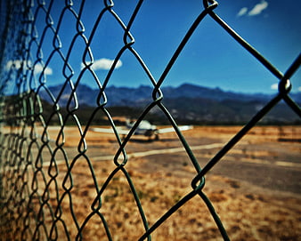 Small airplane on runway seen through chain link fence