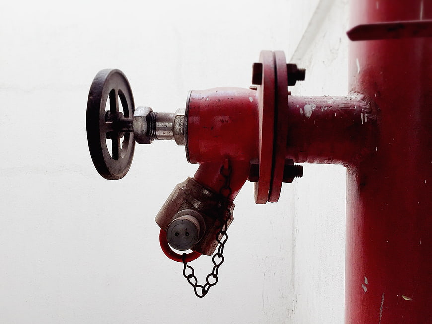 Close-up of red industrial fire hydrant valve on white wall