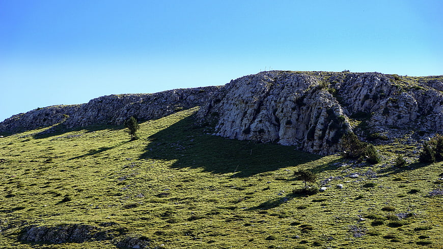 Rugged limestone mountain ridge with green meadow and blue sky