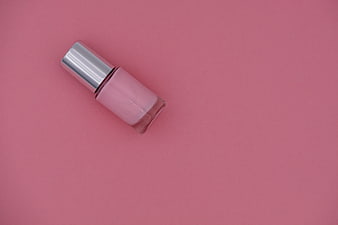 Pink nail polish bottle with silver cap on pink background