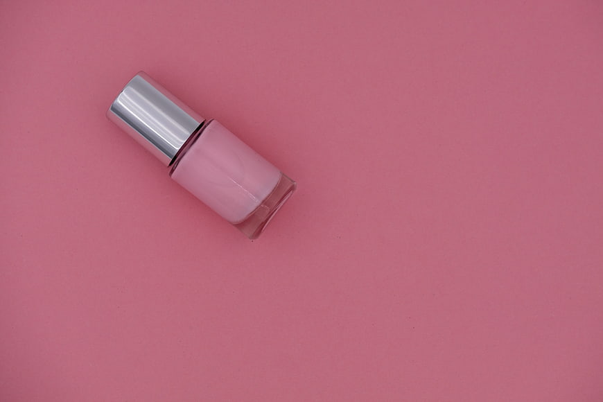 Pink nail polish bottle with silver cap on pink background
