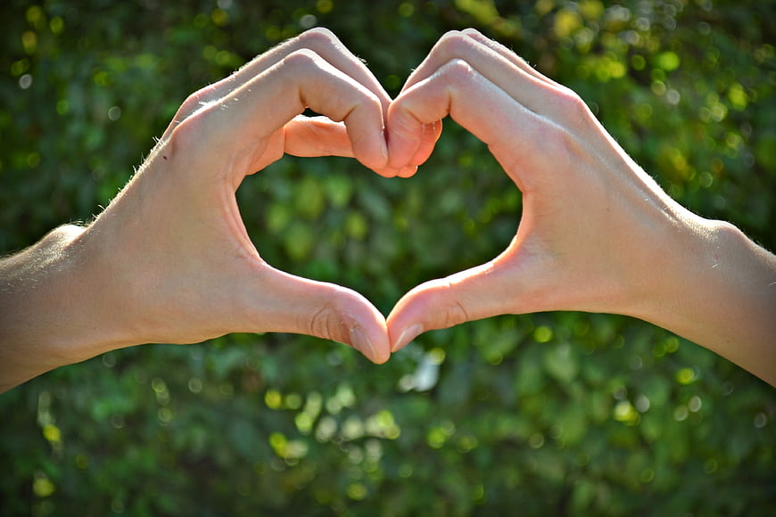 Hands forming heart shape against green bokeh background