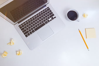 Minimalist workspace with laptop, coffee, and notes on white desk