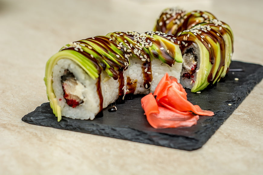 Avocado Topped Sushi Rolls With Sesame Seeds And Ginger On Slate