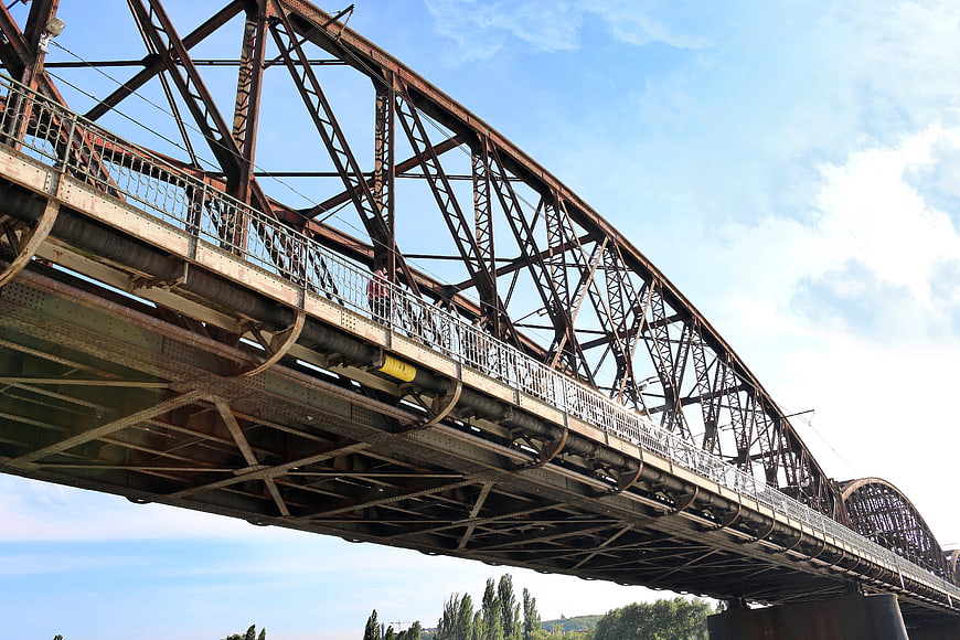 Low angle view of rusty steel truss bridge against blue sky