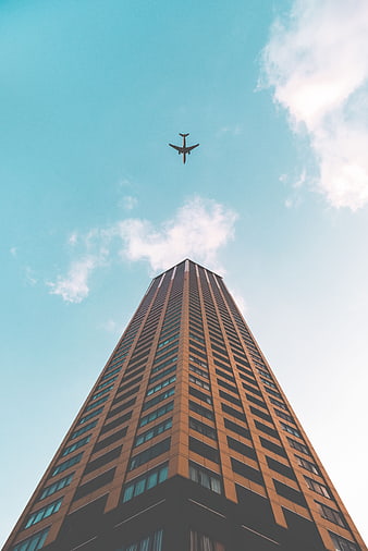 Low angle view of skyscraper with airplane in blue sky