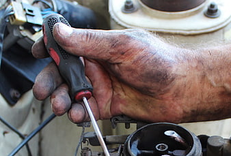 Close-up of dirty mechanic hand using screwdriver on car carburetor
