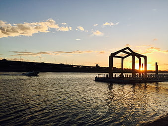 Sunset over water with pier structure and boat silhouette