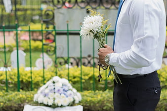 Man holding white flowers and rosary at cemetery grave