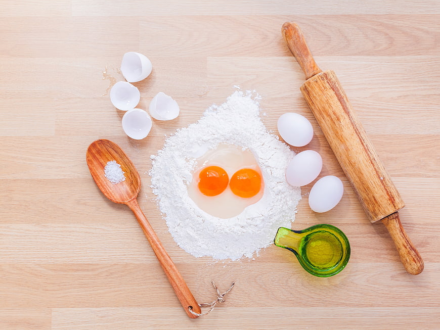 Flat lay of baking ingredients with flour, eggs, and rolling pin