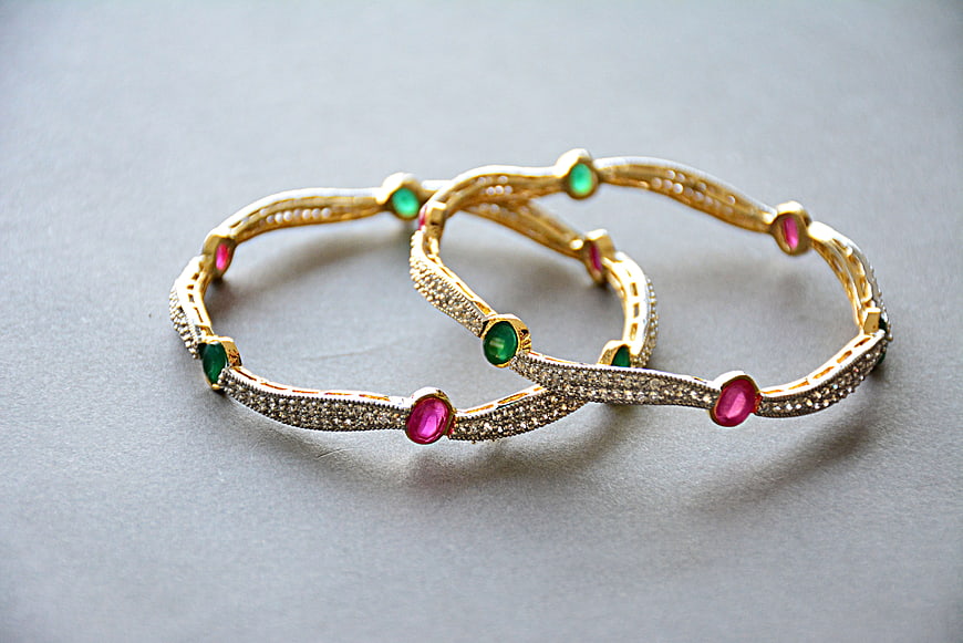 Gold bangles with ruby and emerald gemstones on gray background