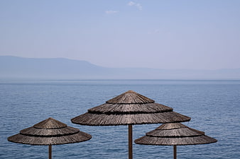 Thatched Beach Umbrellas Against Calm Blue Sea and Distant Mountains