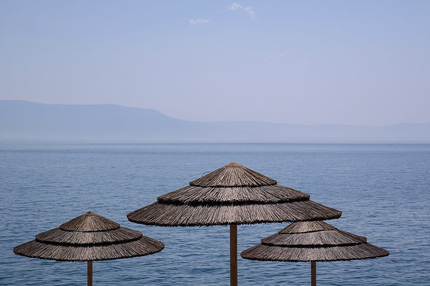 Thatched Beach Umbrellas Against Calm Blue Sea and Distant Mountains