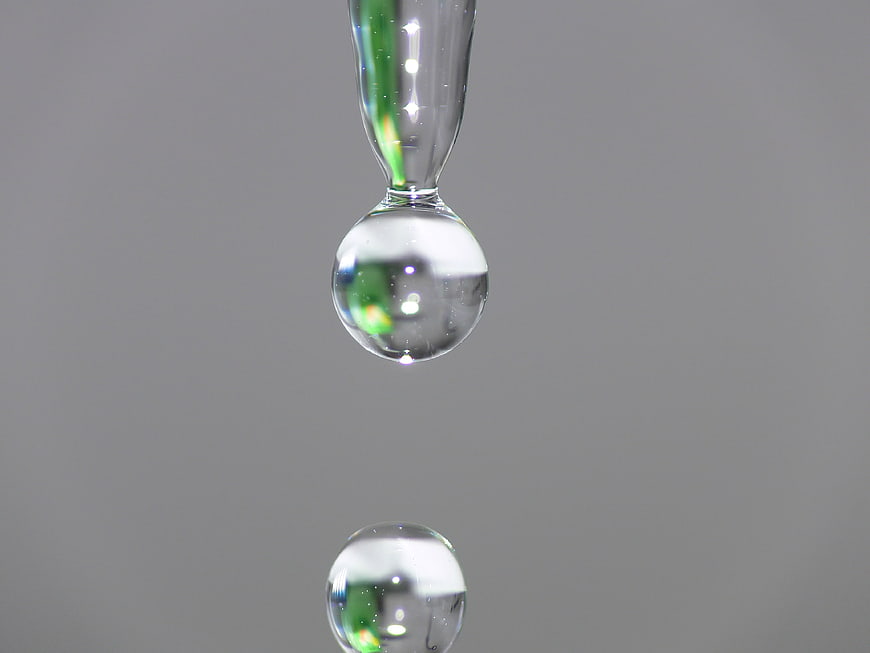Macro shot of clear water droplets falling from a glass pipette