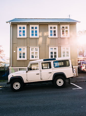 White Land Rover Defender parked in front of a beige wooden building