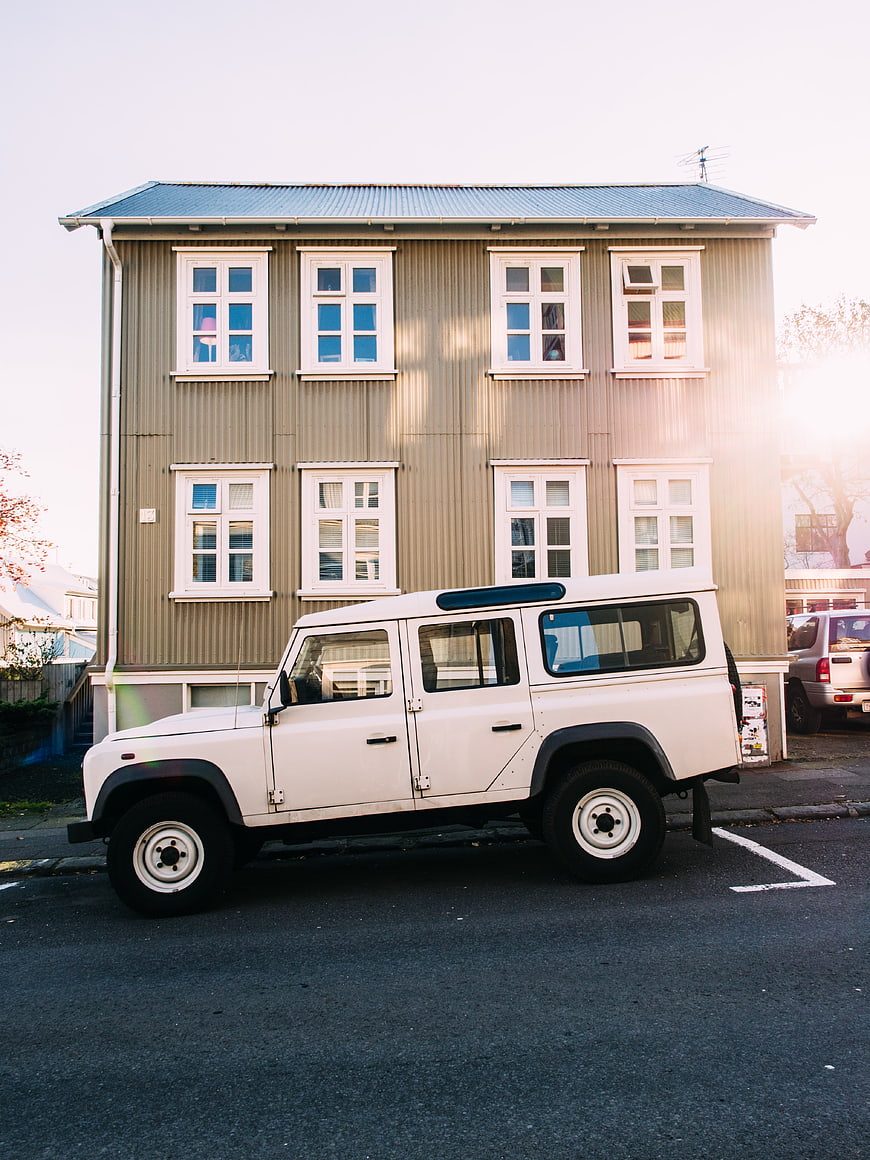 White Land Rover Defender parked in front of a beige wooden building