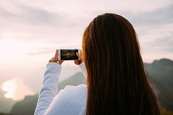 Woman Taking Photo of Sunset Over Mountains with Smartphone