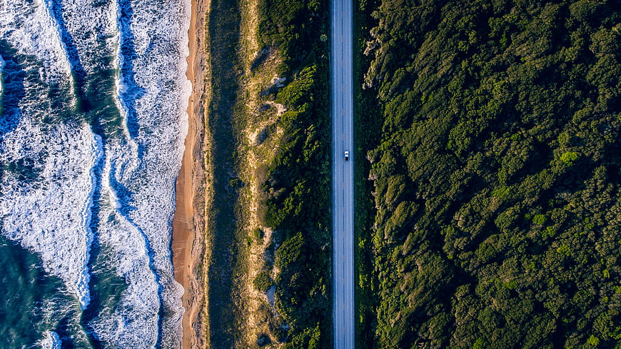 Aerial view of coastal highway with car driving through forest