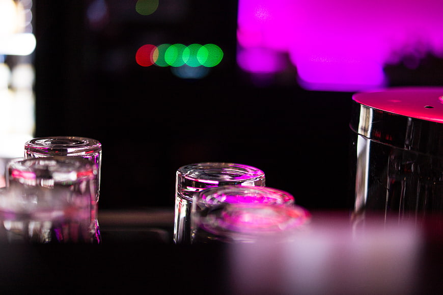 Empty shot glasses on a bar counter with neon bokeh background