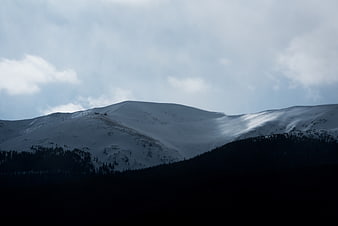 Snowy Mountain Ridge with Dark Forest and Cloudy Sky