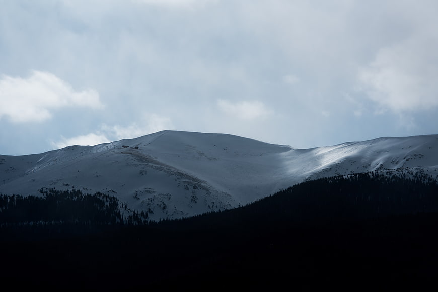 Snowy Mountain Ridge with Dark Forest and Cloudy Sky