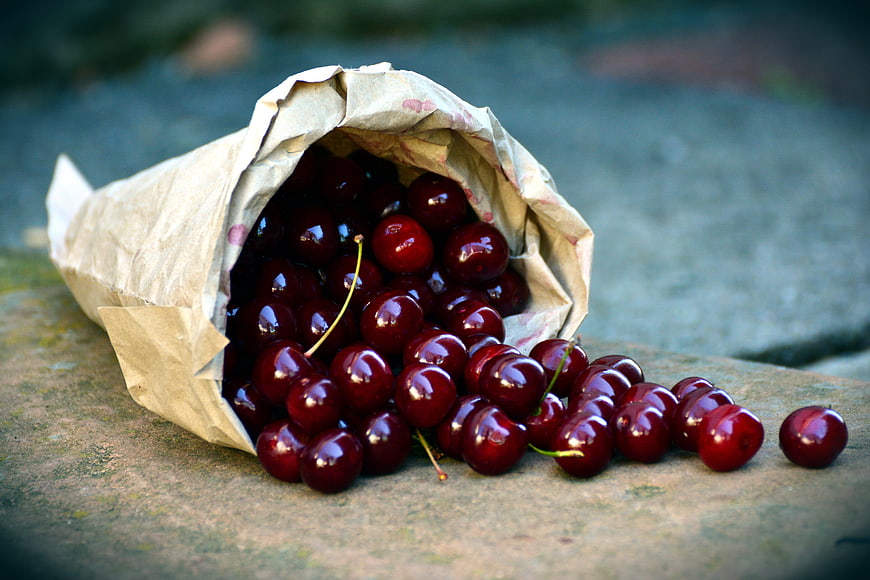 Fresh Ripe Cherries Spilling From A Paper Bag On A Stone Surface